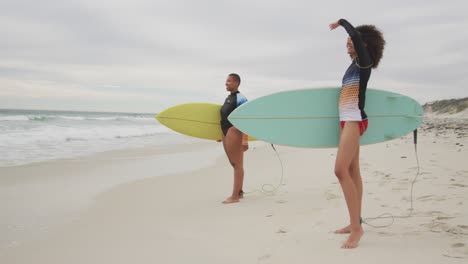 felices amigas afroamericanas en la playa con tablas de surf mirando hacia el mar