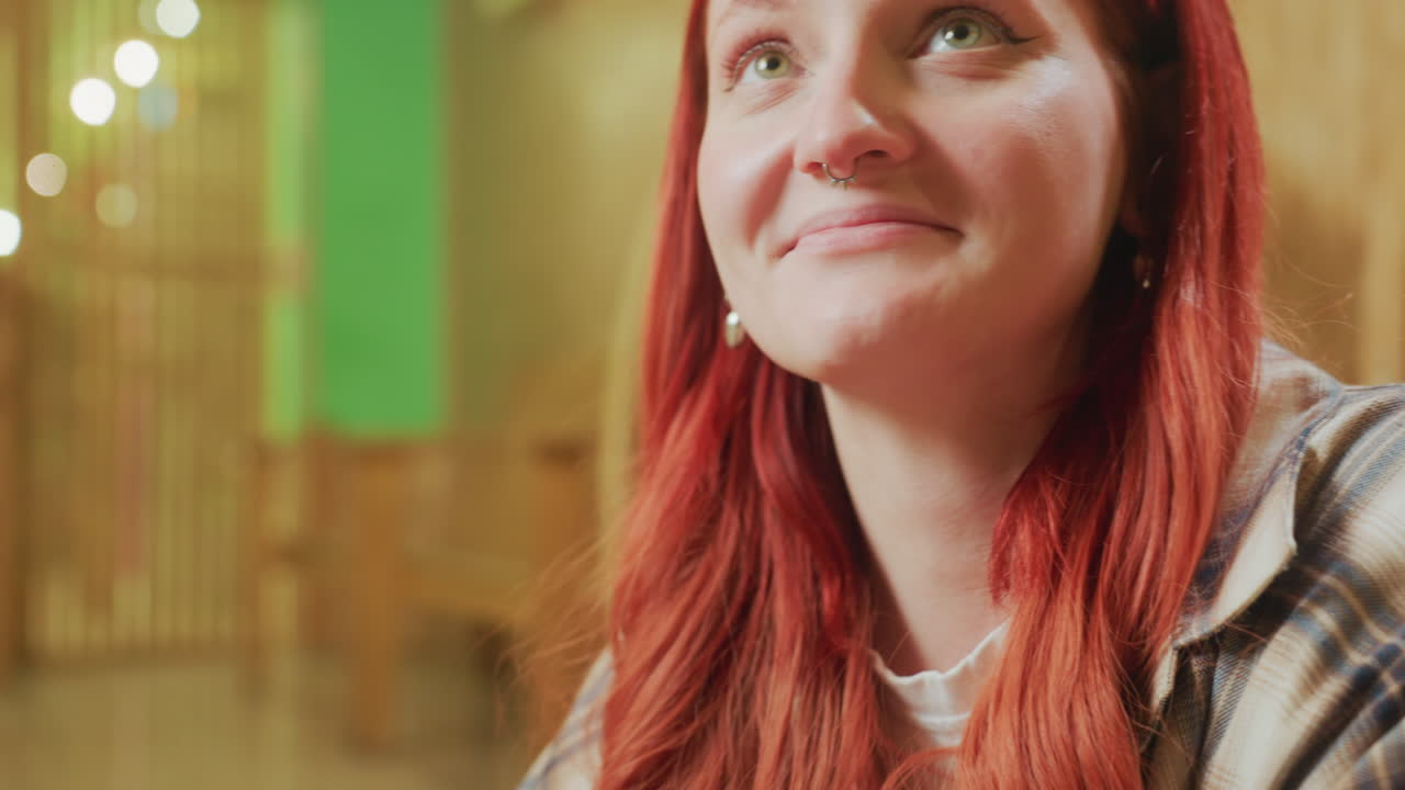 Donna bianca dai capelli rossi sorridente in uno studio accogliente che guarda in su con un sorriso dolce tra luci e archi in legno, controllando gli appunti con espressione soddisfatta, camicia di flanella comoda, momento di speranza per una imprenditrice