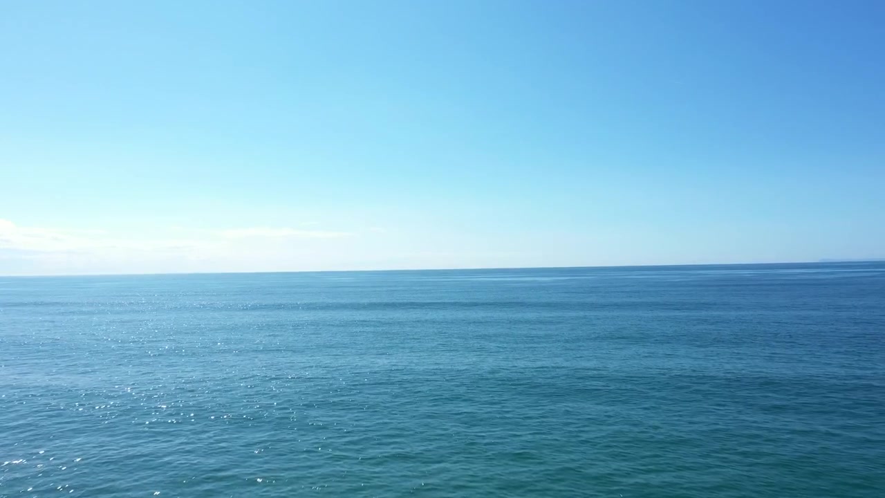 Imagens aéreas movendo-se sobre o mar azul com um horizonte azul, mostrando ondulações na água