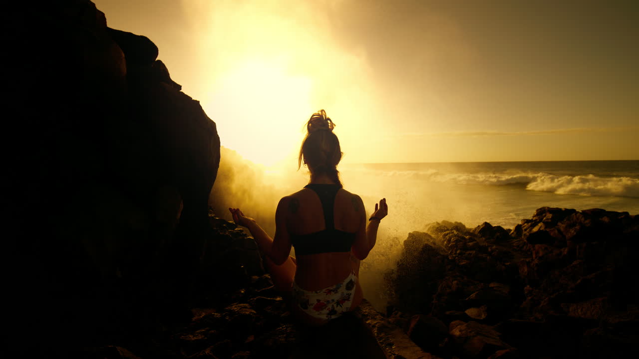 Woman meditating on a volcanic beach during sunset
