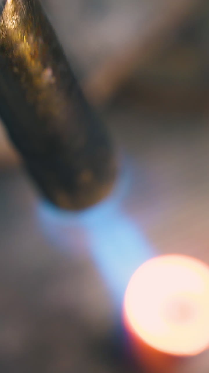 CU: heating of metal detail with hot gas burner blue flame to make jewelry at workplace in dark workshop extreme close upper view
