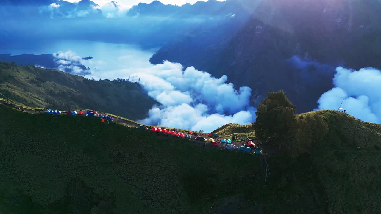 Stunning drone footage shows a high-altitude camping site on the edge of a volcano with a beautiful crater lake below offering breathtaking views and an unforgettable mountain adventure.