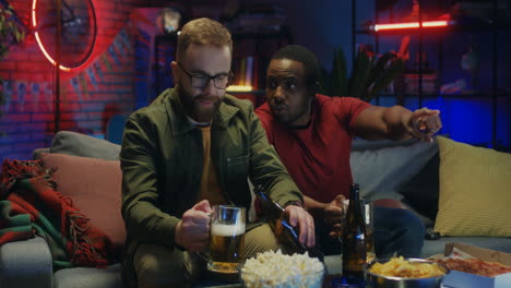 Multiethnic-Two-Good-Looking-Happy-Men-Talking-With-Beer-And-Snacks-Watching-Tv-Together-In-The-Evening-At-Home