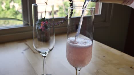 dos copas de champán rosado se vierten en una mesa de cocina junto a la ventana