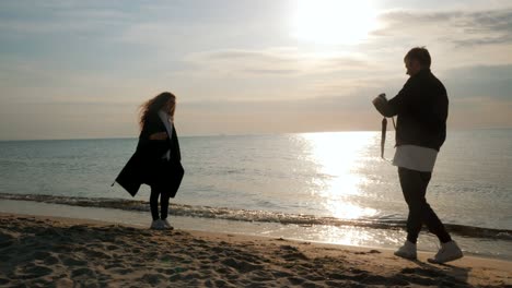 man takes pictures of his beloved on the seashore in spring. photoshoot of beautiful people on the beach. happy married adult couple having fun, playing, fooling. girl posing for guy with camera