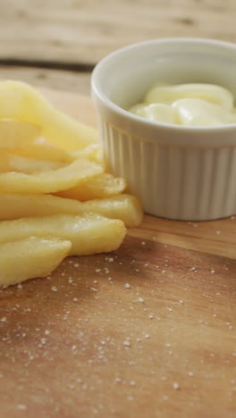 video of fish and chips with lemon wedge and dip on wooden board, on rustic table