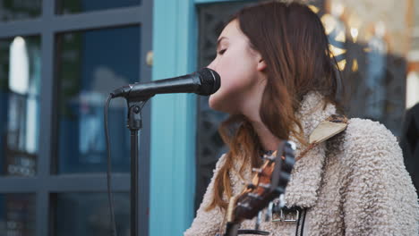 músico femenino tocando la guitarra acústica y cantando al aire libre en la calle