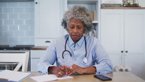 Portrait-of-senior-african-american-female-doctor-talking-notes-while-having-a-videocall-at-home