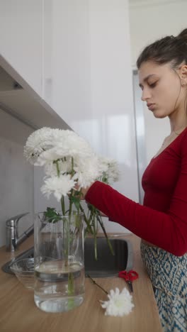 woman arranging white flowers in a kitchen