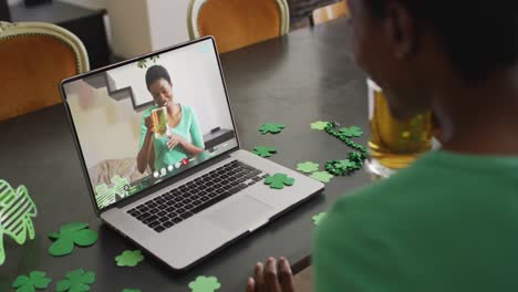 mujer afroamericana sonriente con cerveza vistiendo banda en forma de trébol en una llamada de video en una computadora portátil
