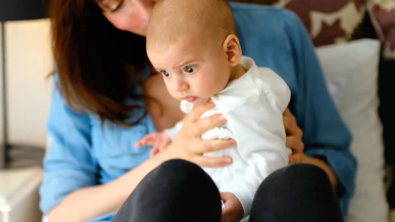 침대에 앉아있는 젊은 엄마는 침실에서 아기를 존경합니다.