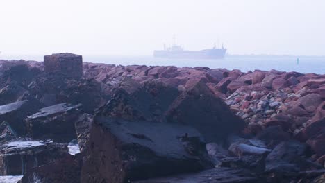 gran buque de carga entrando al puerto de liepaja en un día nublado, muelle de piedra en primer plano, olas salpicando, tiro medio distante