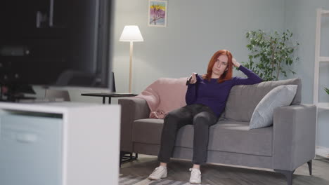 tired redhead woman changes tv channels using remote control