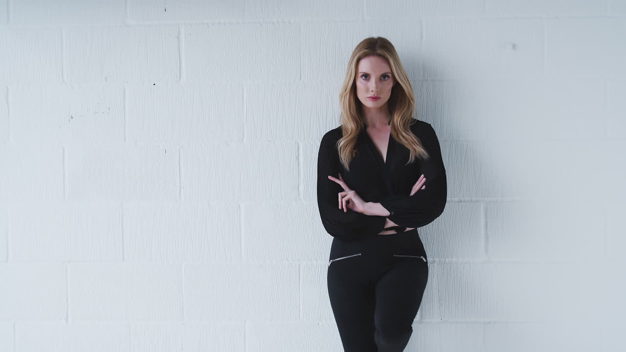 модный портрет серьезной молодой женщины, стоящей на стене белой студии