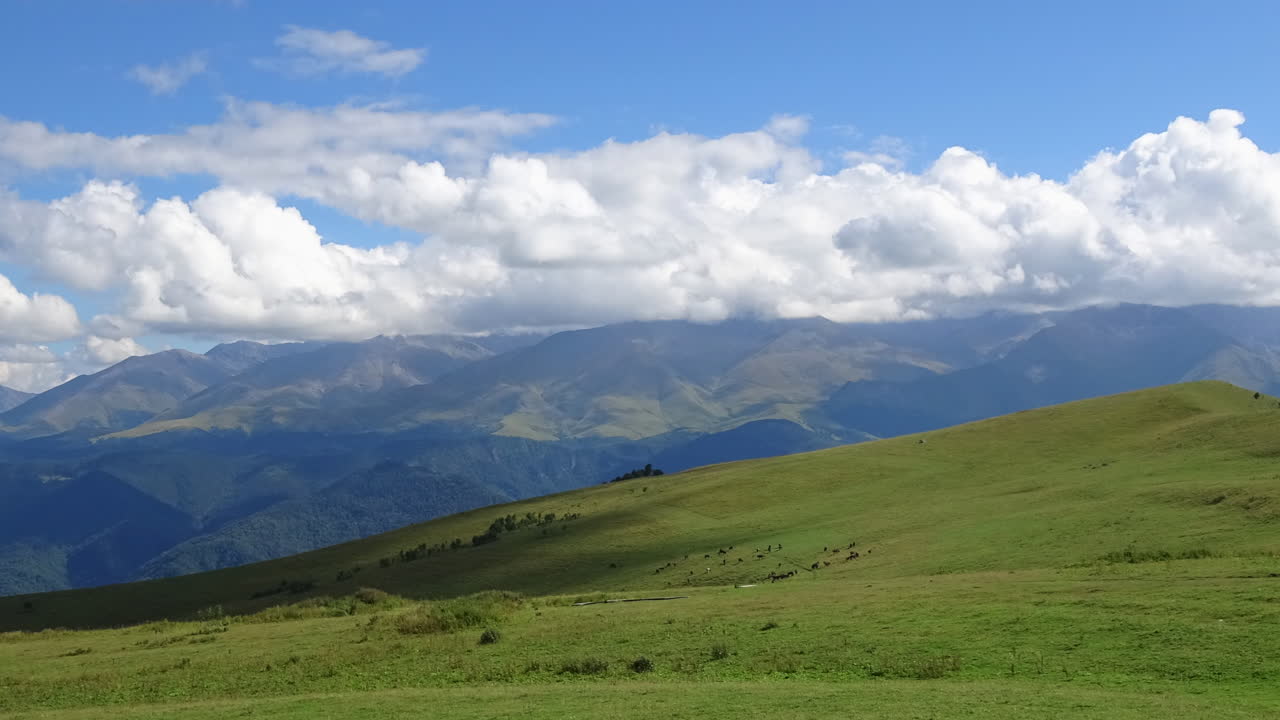 Timelapse di nuvole in rapido movimento che proiettano ombre su un prato alpino verde e un paesaggio stratificato dei Monti del Caucaso, Russia, con un'ampia vista panoramica estiva.