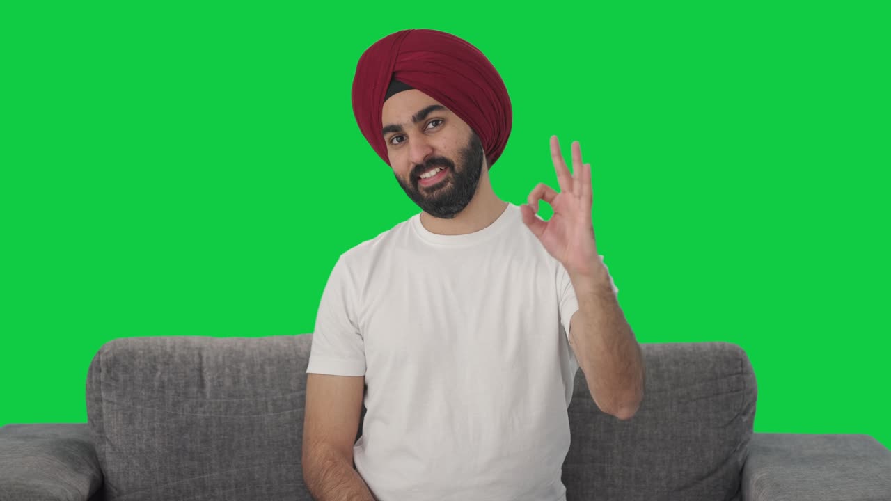 hombre indio sikh feliz mostrando la pantalla verde de la señal de ok