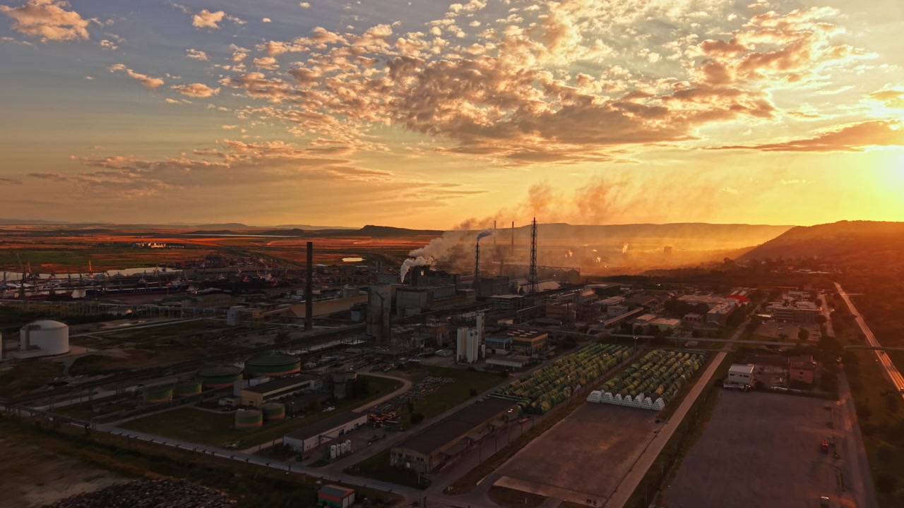 Sunset over industrial area with factories and smoke rising in the sky near a river and fields
