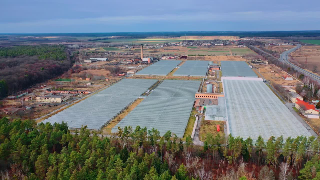 Modern glass greenhouses and industrial buildings in a field near the forest. Aerial view. Shooting in autumn