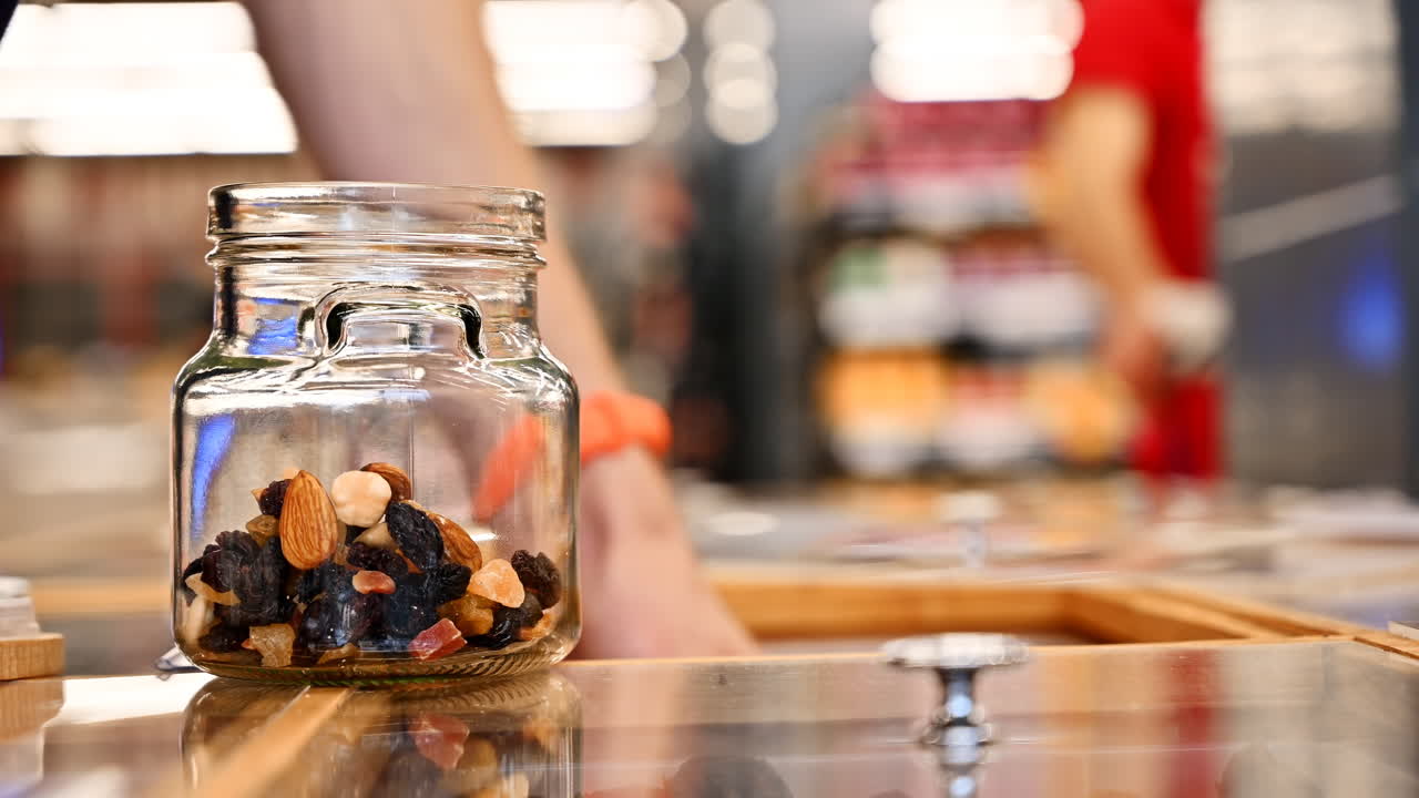 Man's hands filling a glass jar with nuts, dried fruits and berries in supermarket. Ecology idea. Side view