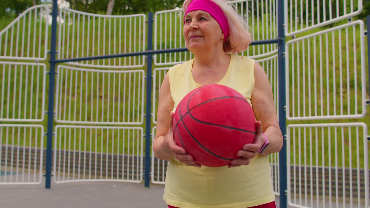 una anciana abuela atleta posando jugando con la pelota al aire libre en la cancha de baloncesto