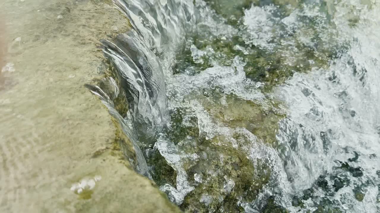 Una vista dinamica in primo piano dell'acqua che scorre e si riversa su una serie di superfici ruvide coperte di muschio delle pietre o rocce.