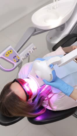 patient receiving professional teeth whitening treatment at dental office using led light. vertical video.