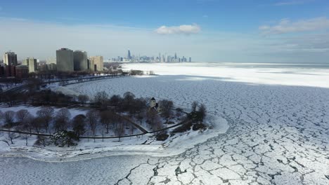 vista aérea sobre el hielo y el punto promontorio con el horizonte de chicago en el fondo, soleado, día de invierno en illinois, ee.uu. - reversa, disparo de drone