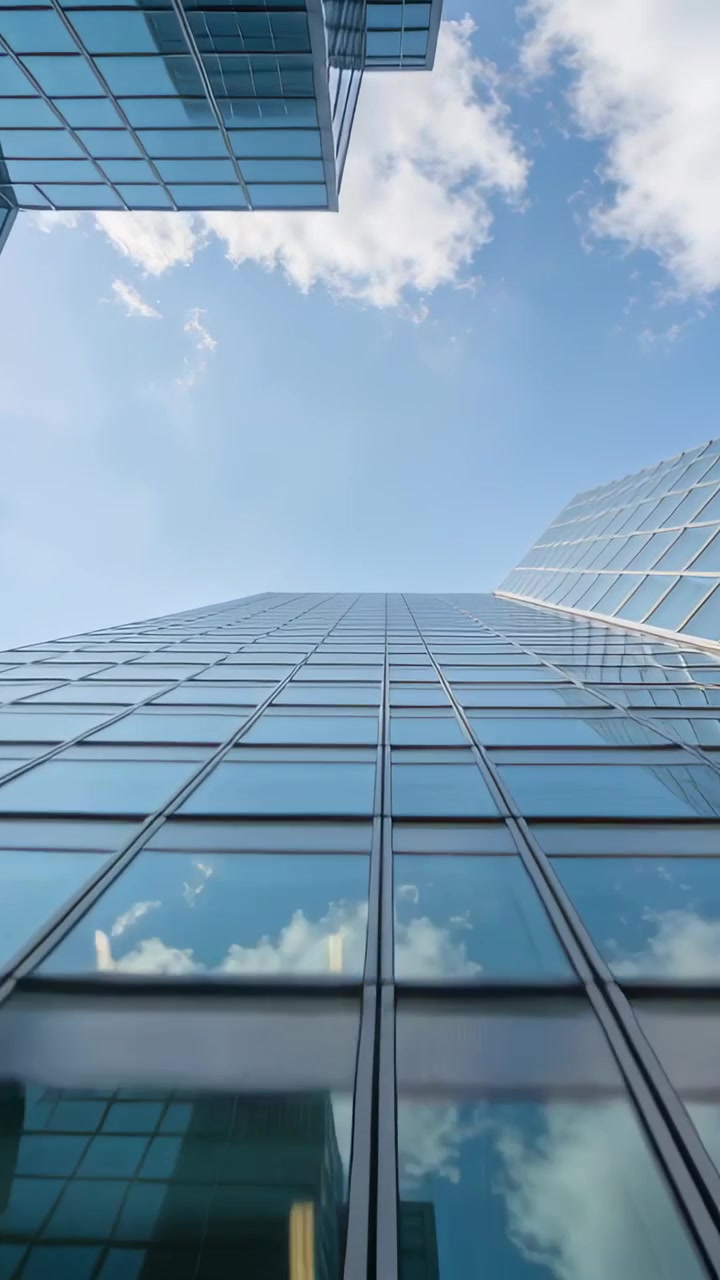 Video vertical: Cámara inclinándose a nivel de la calle siguiendo una torre de cristal hacia arriba mostrando reflejos del cielo.