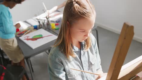 high angle video of concentrating caucasian schoolgirl at easel painting in art class, copy space