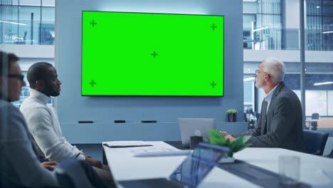 office conference room meeting using video call: diverse team of successful managers, executives talk, use green screen chroma key tv. businesspeople work on strategy for an e-commerce startup