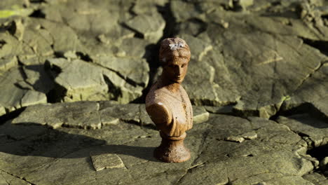 antique bust sculpture on unique cracked earth landscape in bright daylight