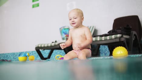 cute blonde toddler is diving under the water in the swimming pool and swimming there until his mother is lifting him from the water