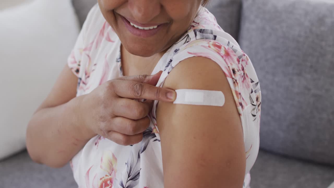 Smiling african american senior woman showing bandage on arm after covid vaccination