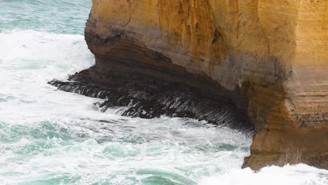 dynamic ocean waves crash against rugged cliffs under natural light at port campbell, creating a dramatic coastal scene