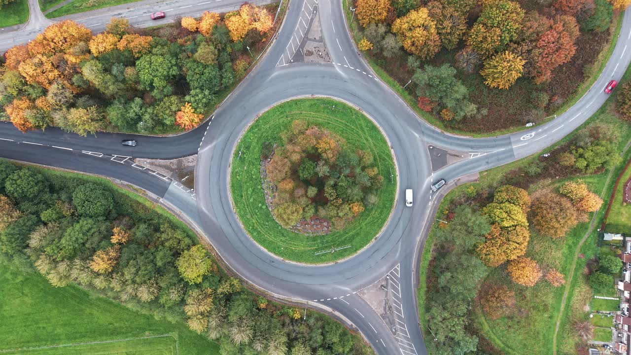 Aerial top down view of a traffic roundabout with cars surrounded by autumn trees