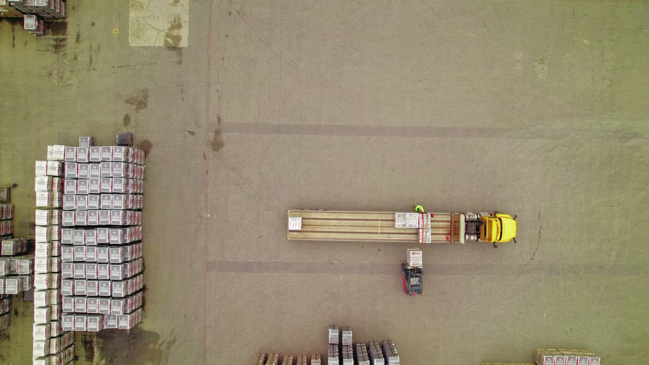 vista aérea de un camión amarillo cargado por carretillas elevadoras en el patio de logística