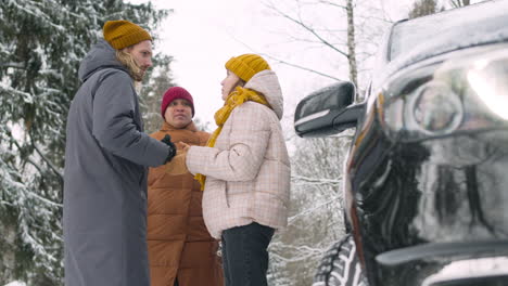 Three-Friends-Standing-Near-The-Car-And-Talking-Together-On-A-Cold-Winter-Day