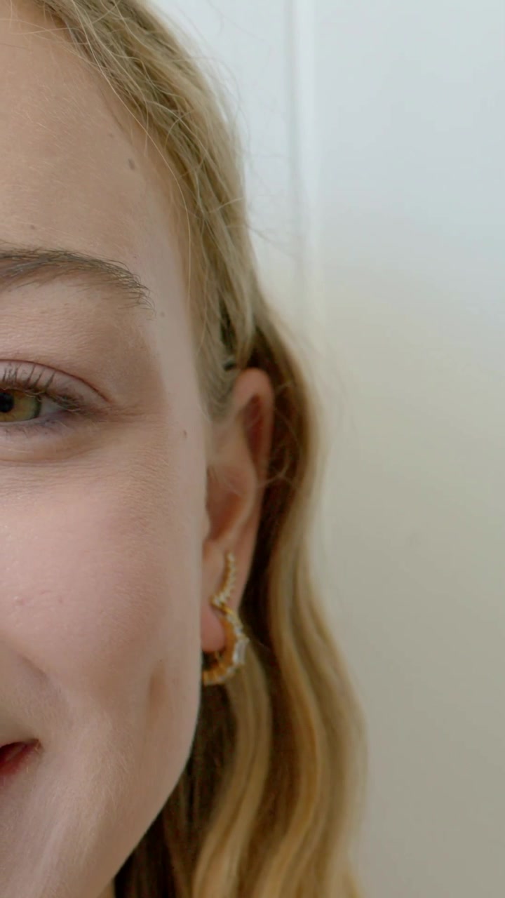 Video verticale: Adolescente che apre l'occhio sinistro e sorride alla telecamera a casa, con orecchino a cerchio d'oro e ear cuff, con spazio per il testo.