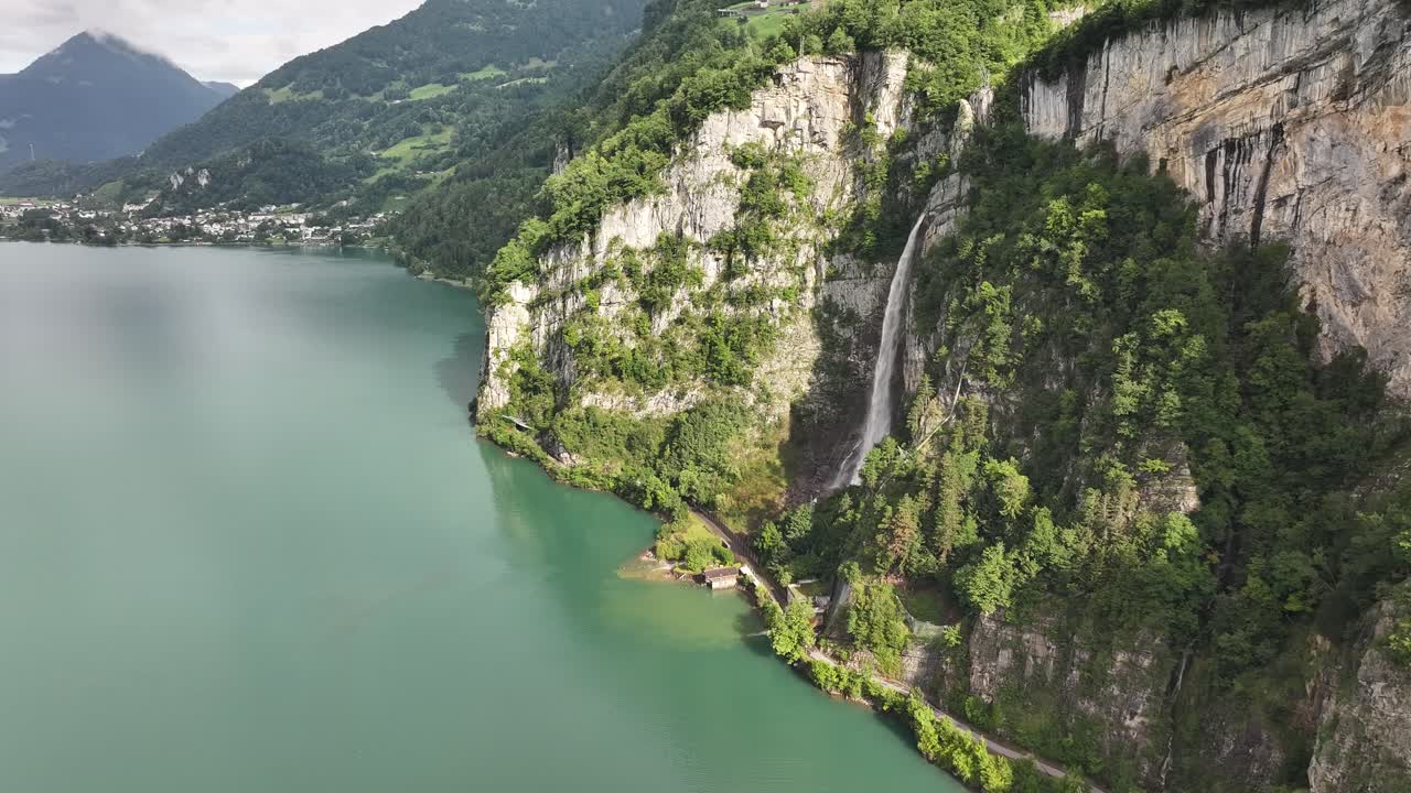 A majestic natural scene captures the Seerenbach Falls cascading down steep, forested cliffs and into the turquoise waters of Walensee in Switzerland. Alpine landscape near Weesen