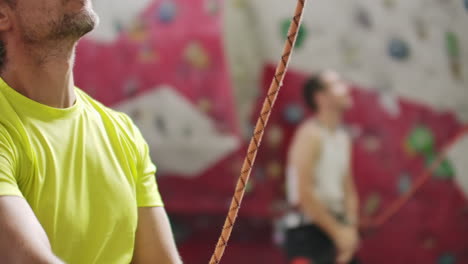 Man-belaying-another-climber-with-rope.-Top-view-of-young-athletic-man-belaying-and-watching-another-climber-with-rope.-Summer-time.-Climbing-equipment.