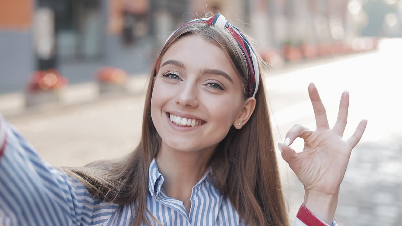Mujer joven feliz saludando y sonriendo durante una videollamada selfie.