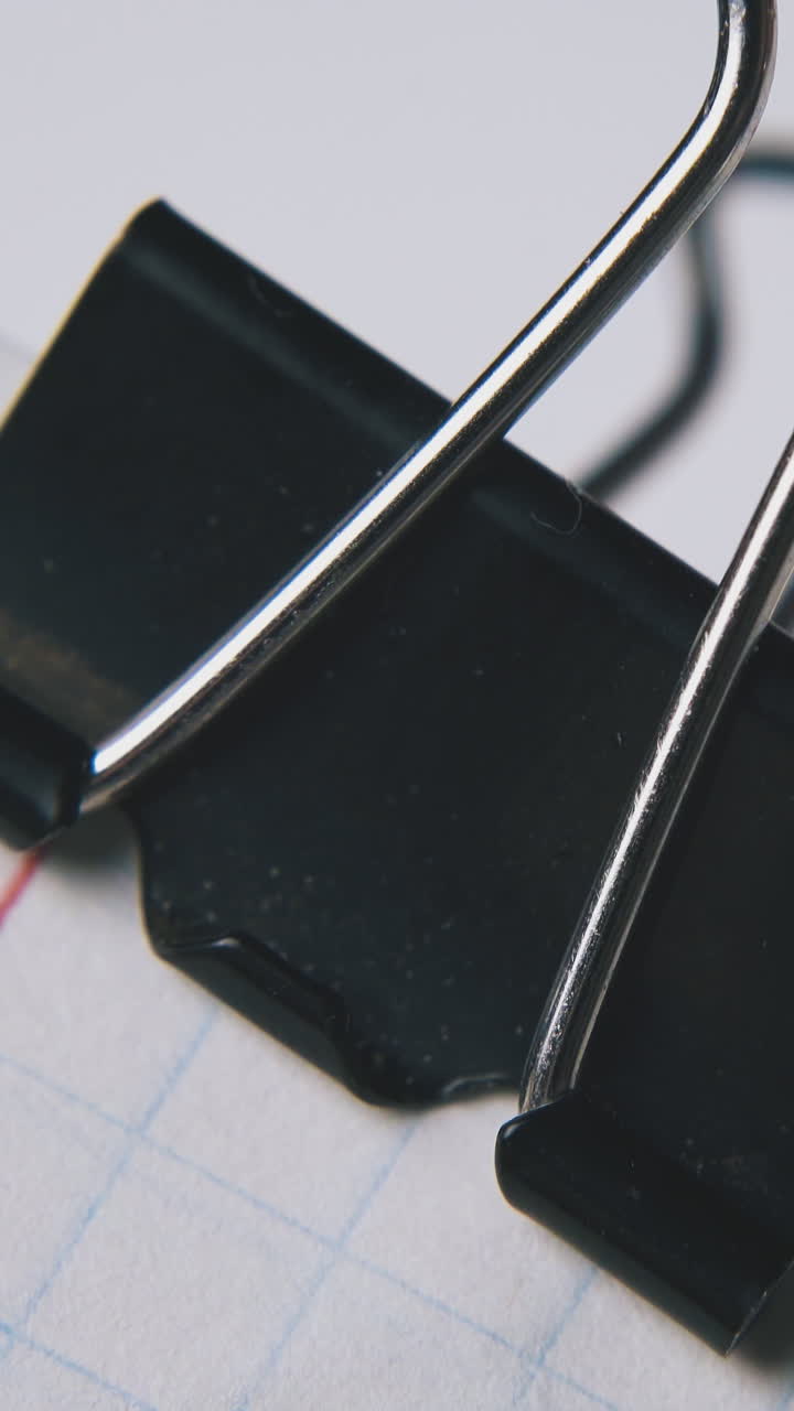 person takes off black clamp from checkered paper sheets on white background extreme close view
