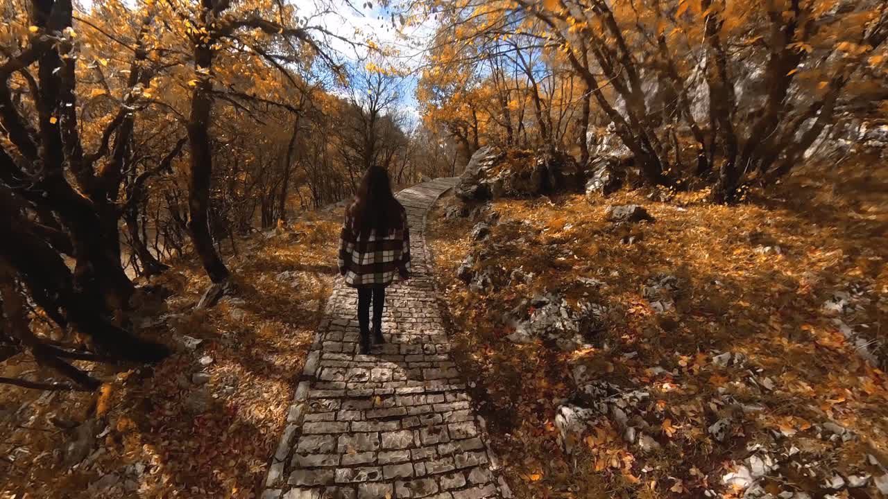chica caminando por un camino pavimentado de piedra en las colinas rodeadas de hojas de otoño que se vuelven naranjas