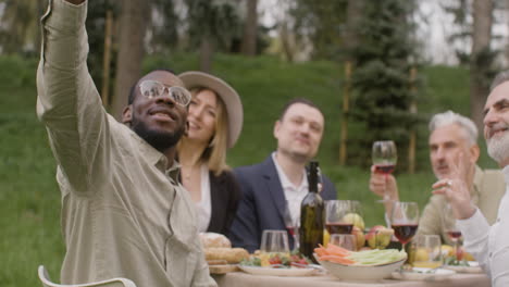 group of middle aged friends taking a selfie sitting at table during an outdoor party in the park 1