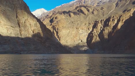 cielo azul sobre las nubes blancas mirando el hermoso agua azul del lago sobre la roca y las montañas nevadas, haciendo que el oro brille en el agua, la gente con una vista impresionante con un barco sobre el lago