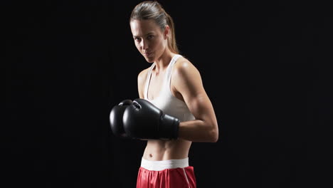 young caucasian woman boxer in boxing gear poses confidently on a black background