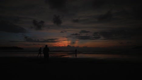 Statische-Zeitrafferaufnahme-Eines-Sees-Mit-Ruhigem-Wasser-Mit-Menschen,-Die-Während-Eines-Wunderschönen-Sonnenuntergangs-Mit-Vorbeiziehenden-Wolken-Am-Ufer-Spazieren-Gehen