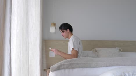 Mann-Schreibt-SMS-Am-Telefon,-Während-Er-Auf-Dem-Bett-Sitzt