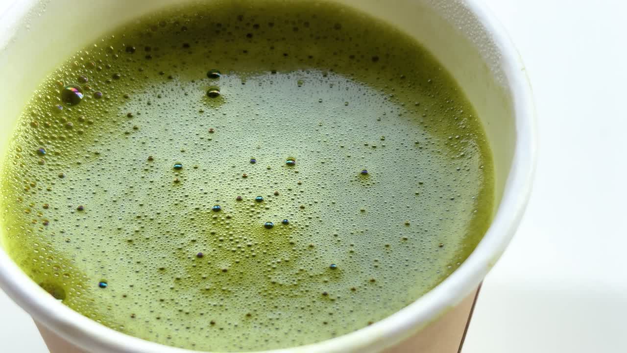 Uma tomada em close-up de ângulo alto de um vibrante matcha latte verde ou um smoothie verde rico em nutrientes servido em um copo de papel branco para viagem