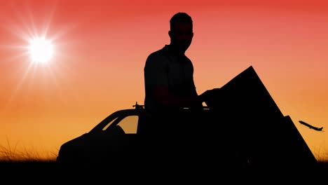 animation of silhouetted delivery man with trolley moving over van and plane on orange sky